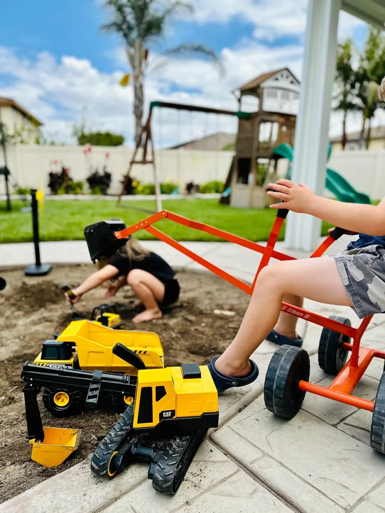 Kids playing in the dirt and on excavator toy in the backyard play area for kids.