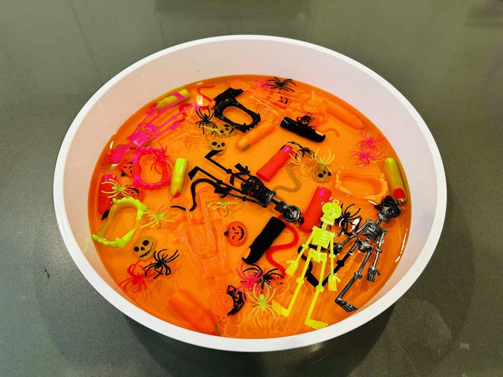 Adding Halloween toys to liquid Jello to create a Halloween Jello Sensory Bin.