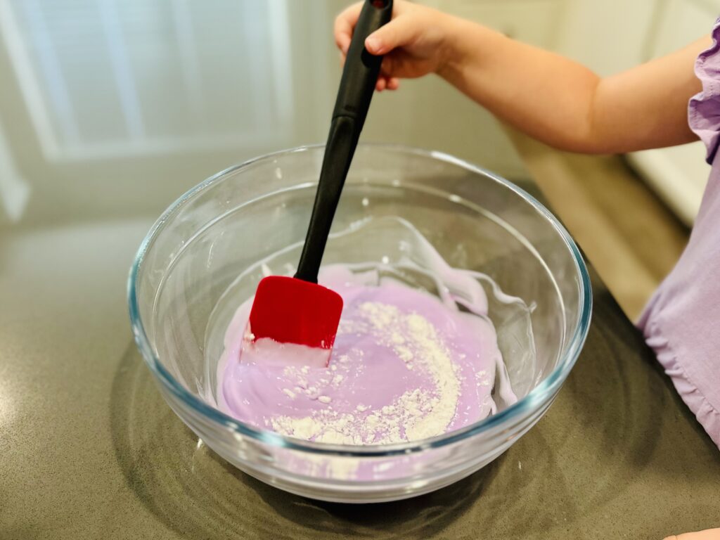 Child mixing the baking soda in a mixing bowl to make homemade slime.